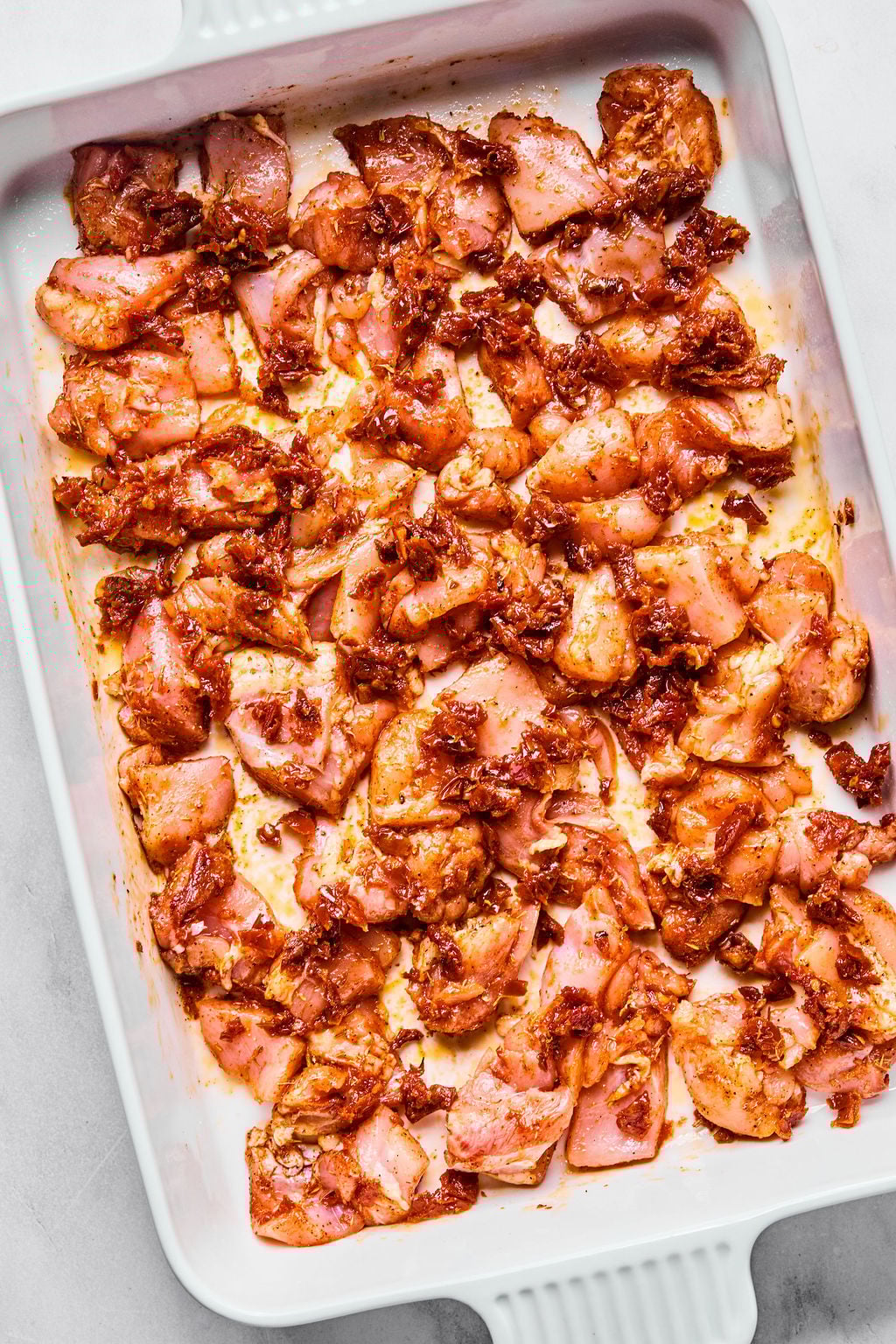 Raw, marinated chicken pieces spread evenly in a white baking dish, ready for cooking.