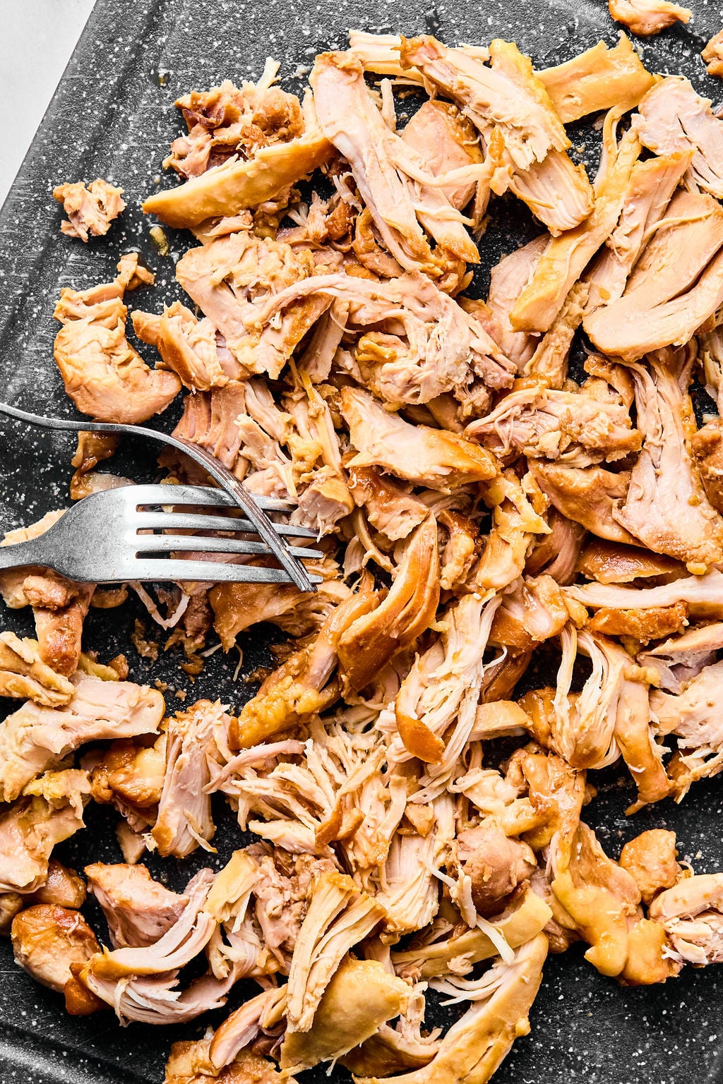 Shredded cooked chicken being pulled apart with a fork on a dark surface.