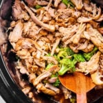 Shredded cooked chicken and broccoli in a slow cooker with a wooden spoon.