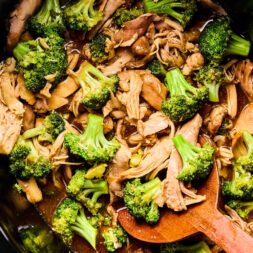Chicken and broccoli cooked in a savory sauce inside a slow cooker, with a wooden spoon stirring the mixture.