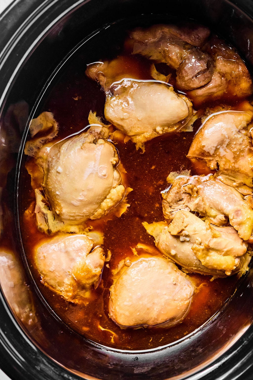 Chicken thighs simmering in a slow cooker with a dark brown sauce.
