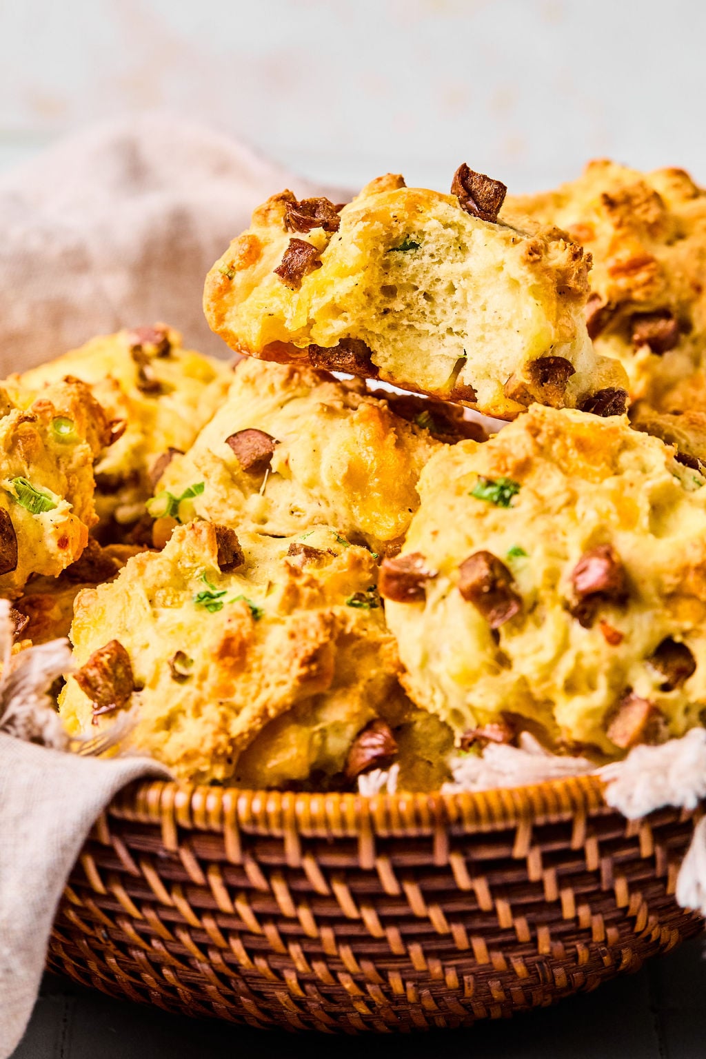 A basket filled with cheddar and bacon biscuits, with one biscuit broken in half showing its soft interior.