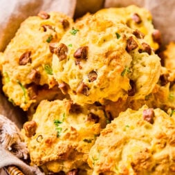 A basket filled with savory biscuits containing chopped herbs and pieces of sausage.