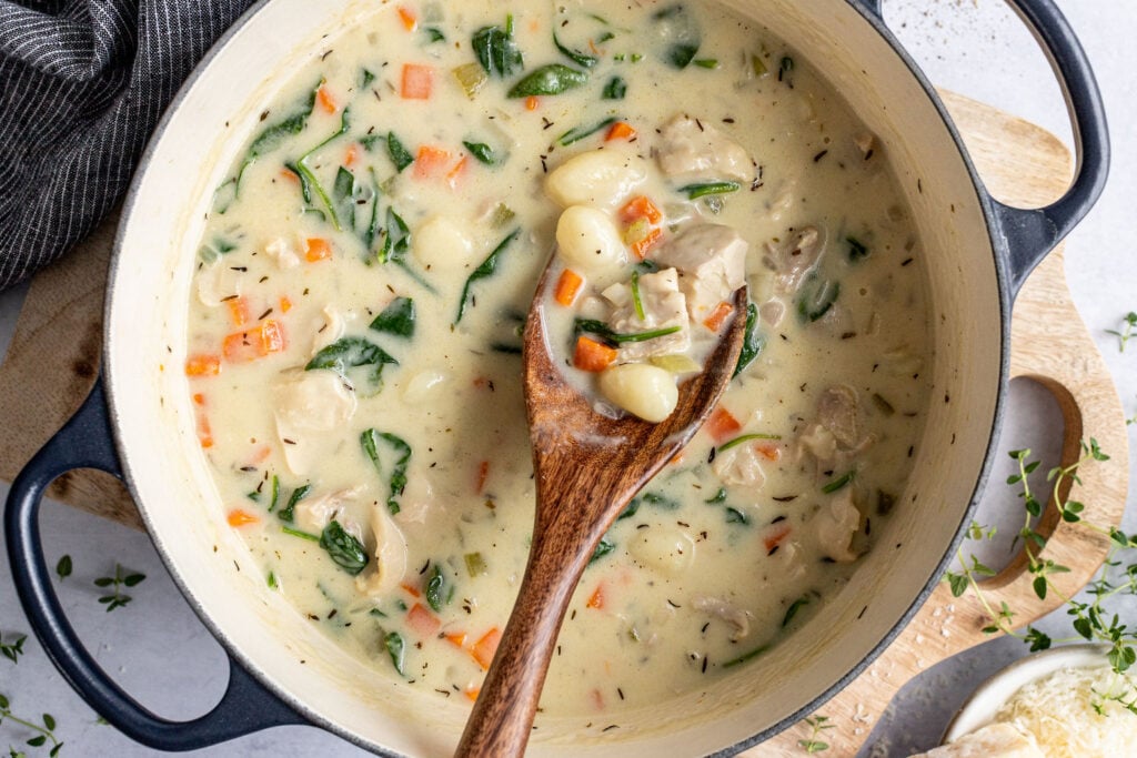 A pot of creamy soup with gnocchi, chicken, spinach, carrots, and herbs.
