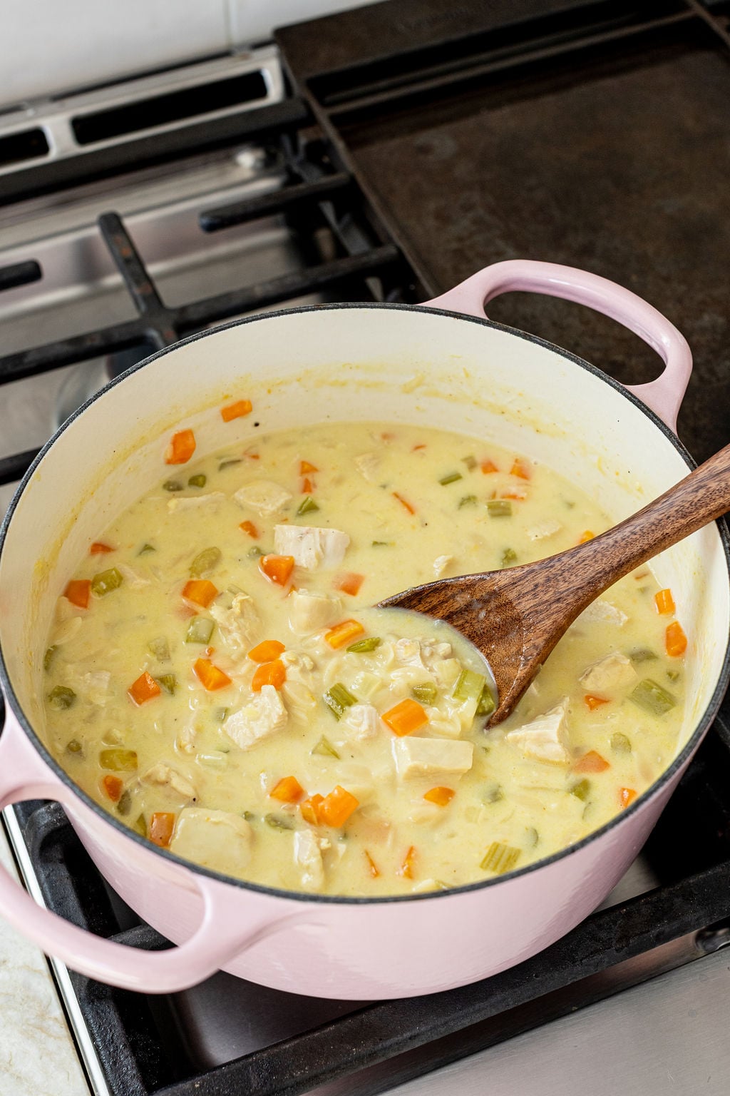 A Dutch oven on a stove contains a creamy soup with chunks of chicken, carrots, and celery.