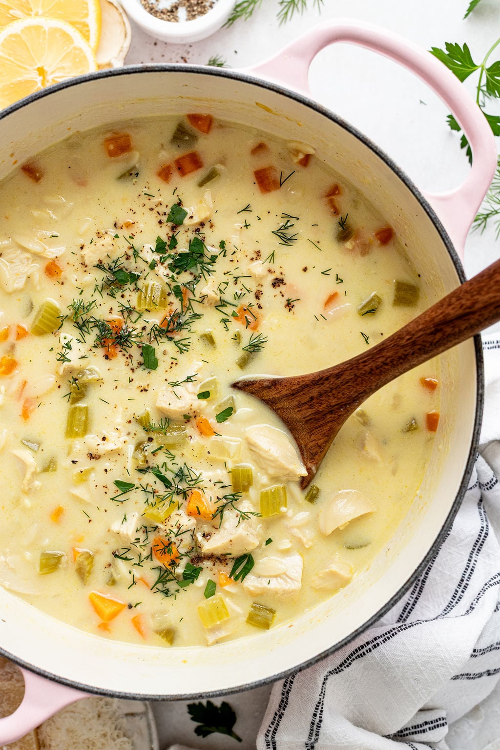 A pot of creamy chicken and vegetable soup with chopped carrots, celery, and herbs, stirred with a wooden spoon.