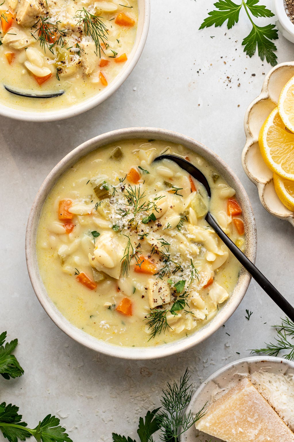 Two bowls filled with chicken and orzo soup with chopped vegetables and fresh herbs.
