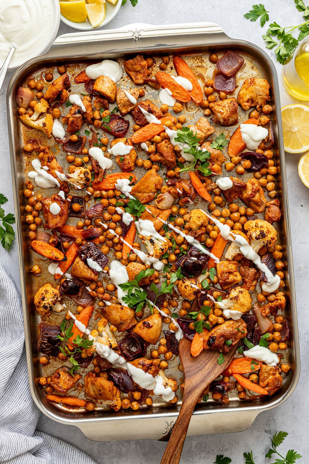 Roasted vegetables and chicken on a baking sheet drizzled with creamy white sauce.