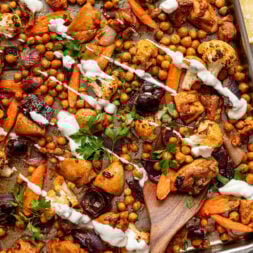 Roasted chickpeas, chicken, and vegetables drizzled with yogurt sauce on a sheet pan.