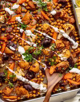 Roasted chickpeas, chicken, and vegetables drizzled with yogurt sauce on a sheet pan.