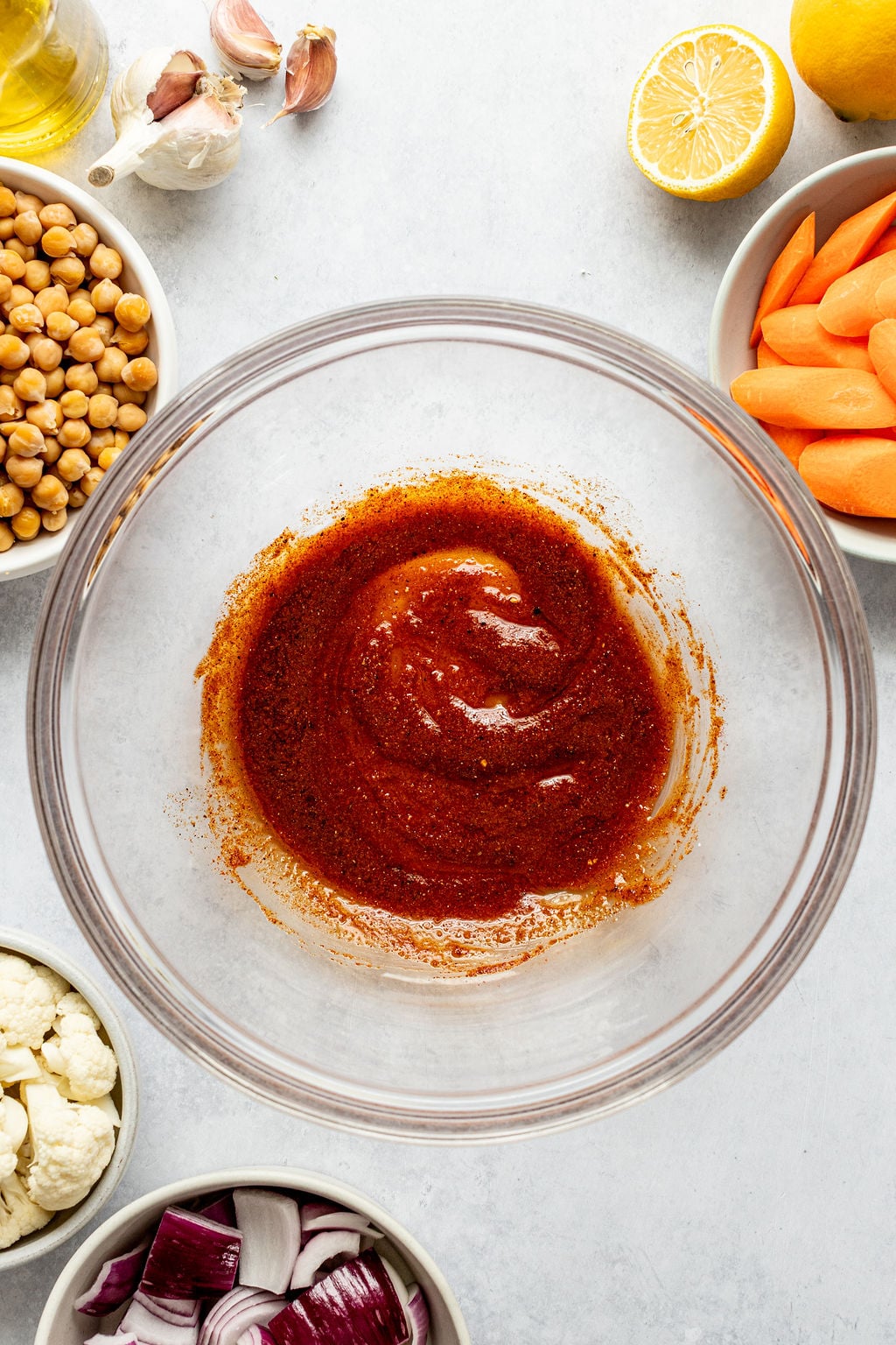 A bowl with cream red sauce next to bowls of carrots, chickpeas, and cauliflower.