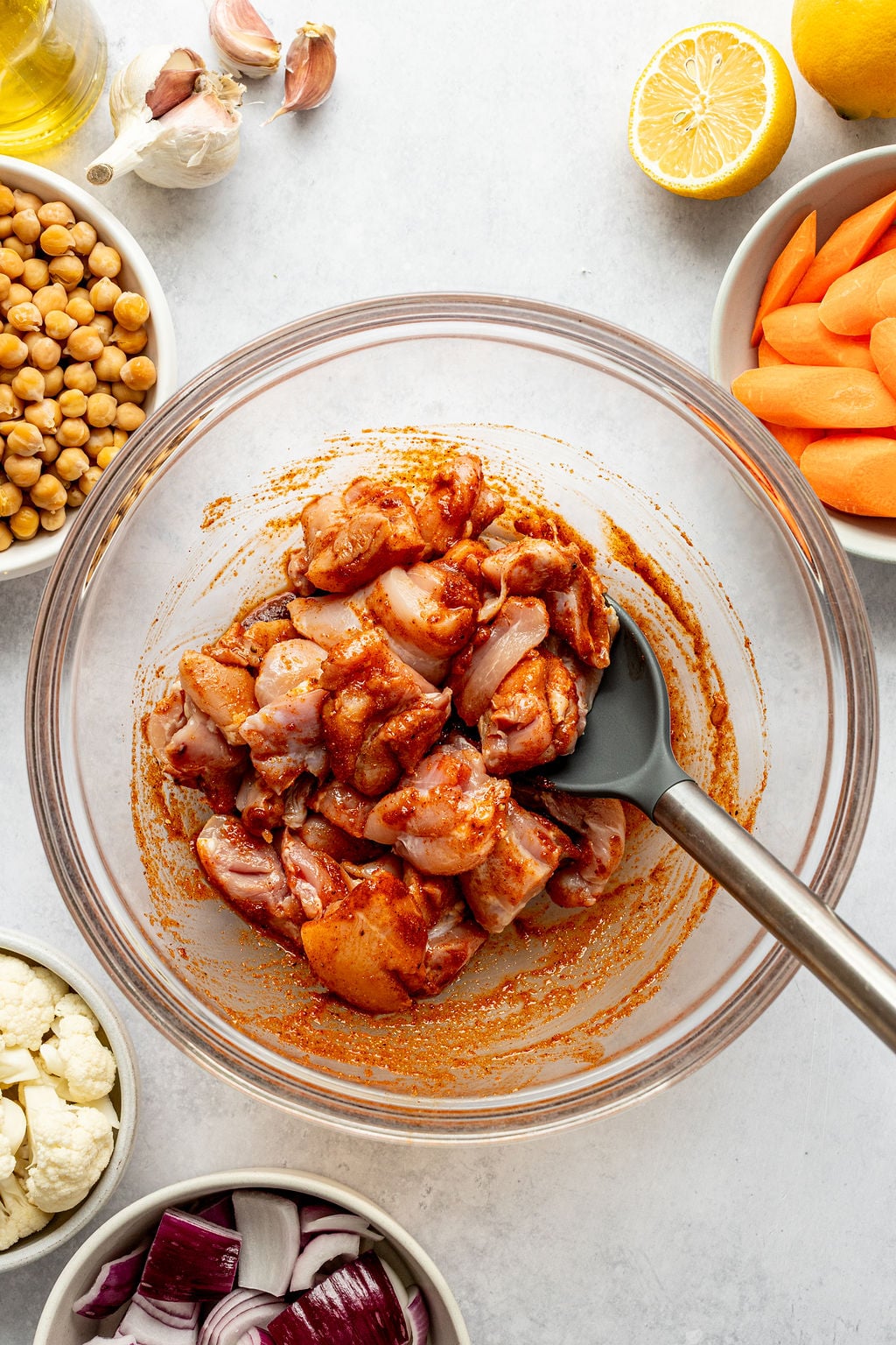 A spoon mixing raw cubed chicken in red sauce.