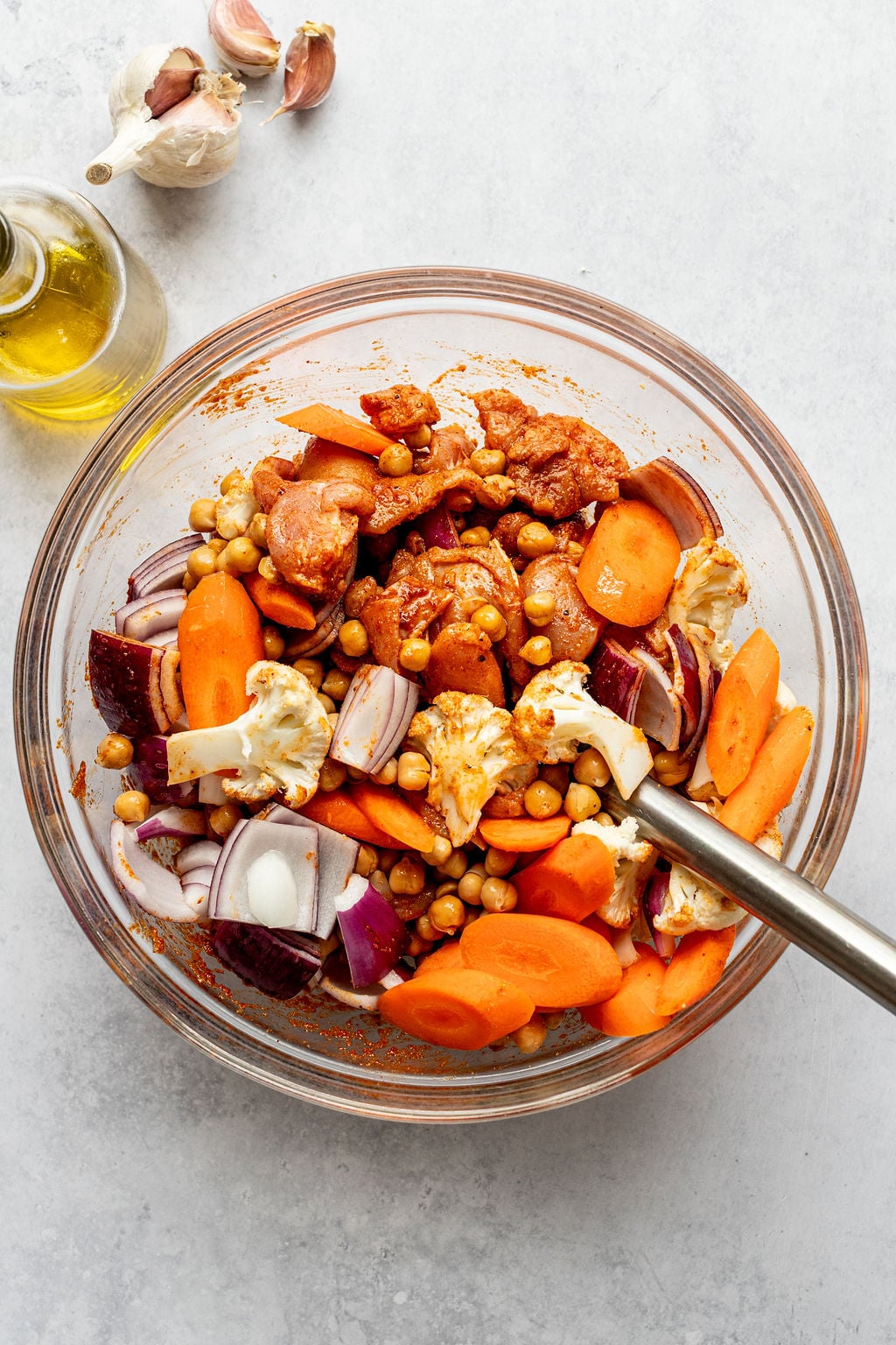 A metal spoon mixing chopped vegetables and chickpeas in a dark red sauce.