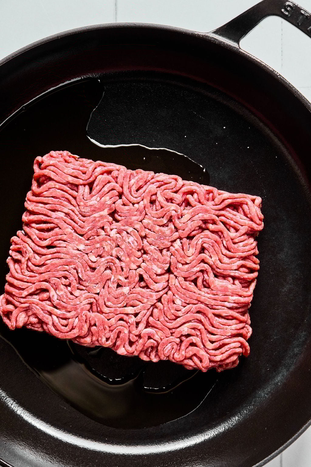 Raw ground beef sits in a black cast iron skillet with a small amount of oil.