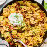 A skillet filled with cabbage and ground beef pasta topped with a dollop of sour cream and sprinkled with chopped parsley.