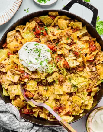 A skillet filled with cabbage and ground beef pasta topped with a dollop of sour cream and sprinkled with chopped parsley.