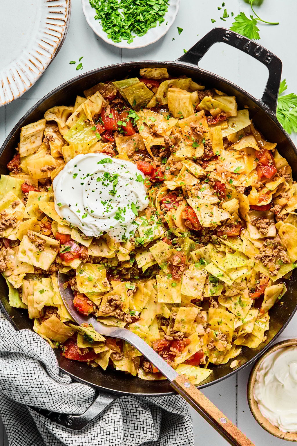 A skillet filled with cabbage and ground beef pasta topped with a dollop of sour cream and sprinkled with chopped parsley.