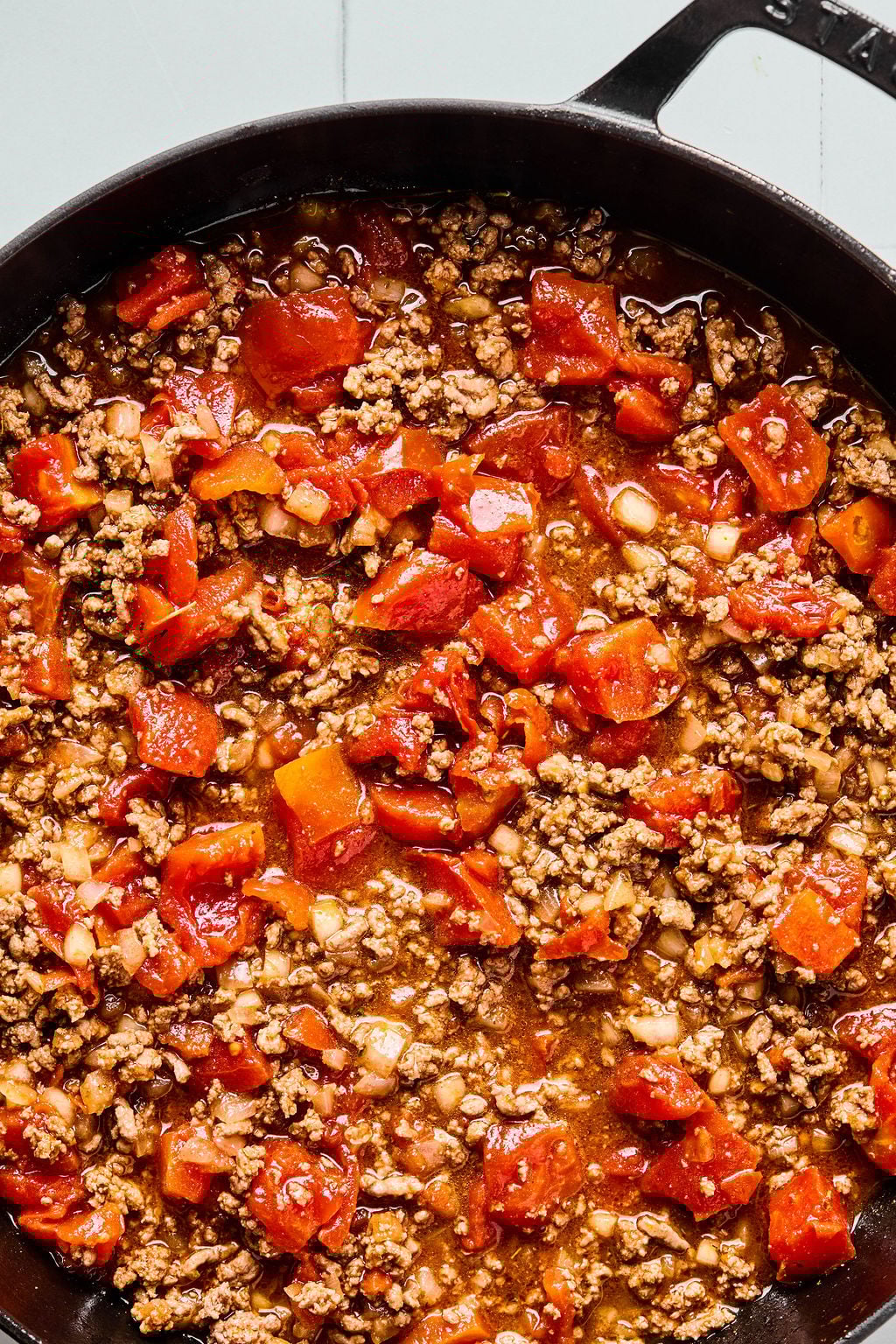 A close-up of a skillet filled with cooked ground beef, diced tomatoes, onions, and spices.