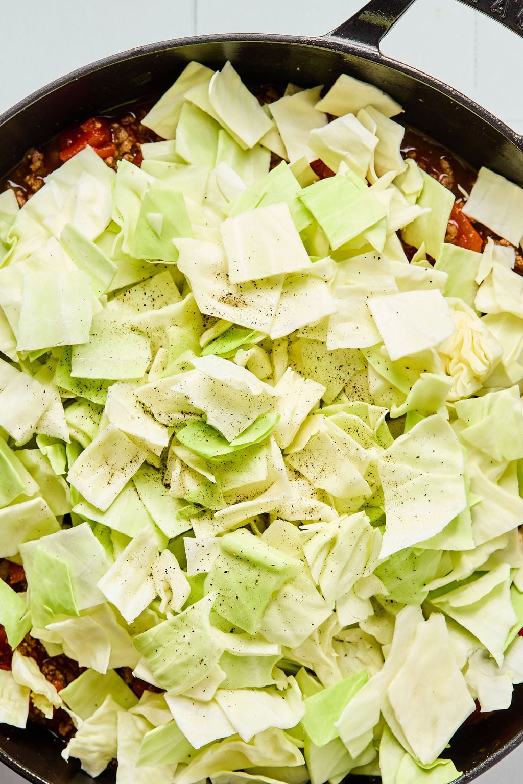 Chopped raw cabbage pieces seasoned with black pepper in a skillet, ready to be cooked.