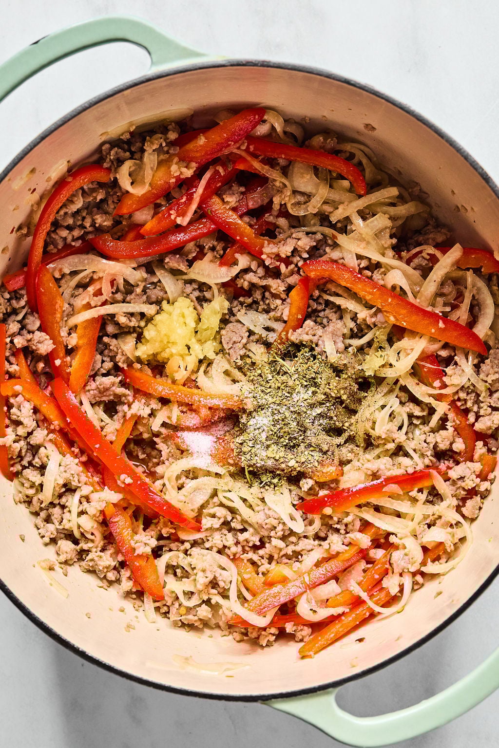 A pot containing cooked ground meat, sliced red bell peppers, onions, and seasonings.