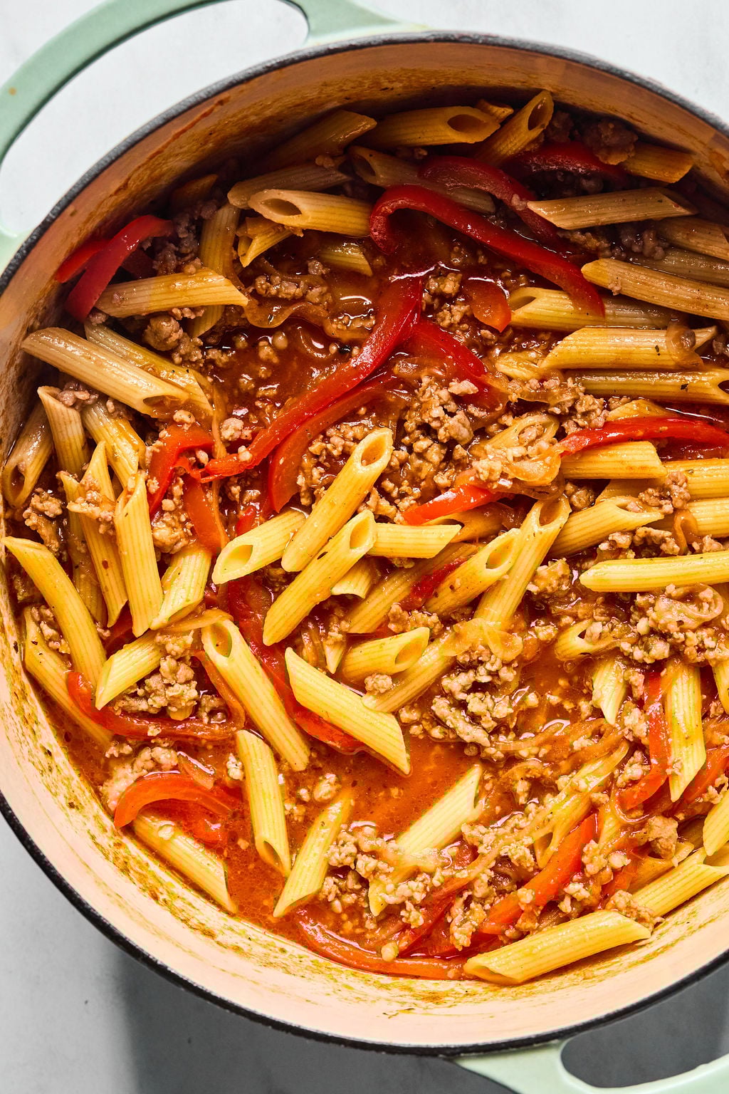 A pot filled with cooked penne pasta, ground meat, red bell pepper strips, and a tomato-based sauce.