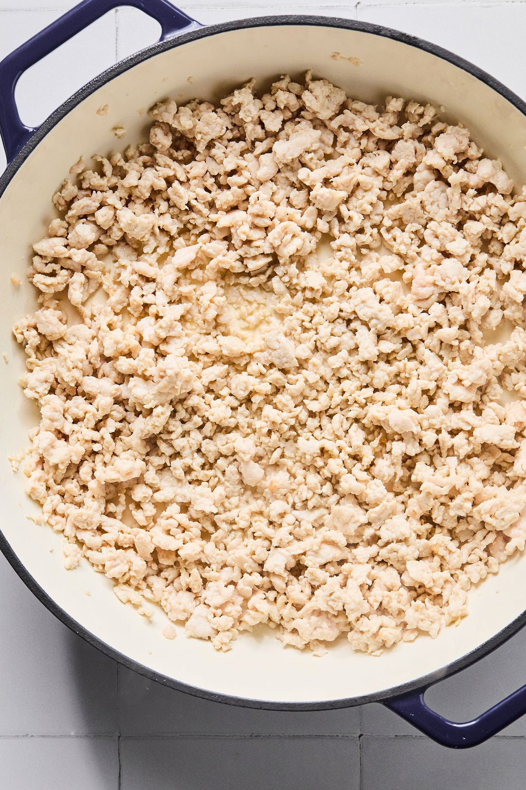 Cooked ground turkey in a large white pot with a dark blue handle, placed on a light-colored tiled surface.