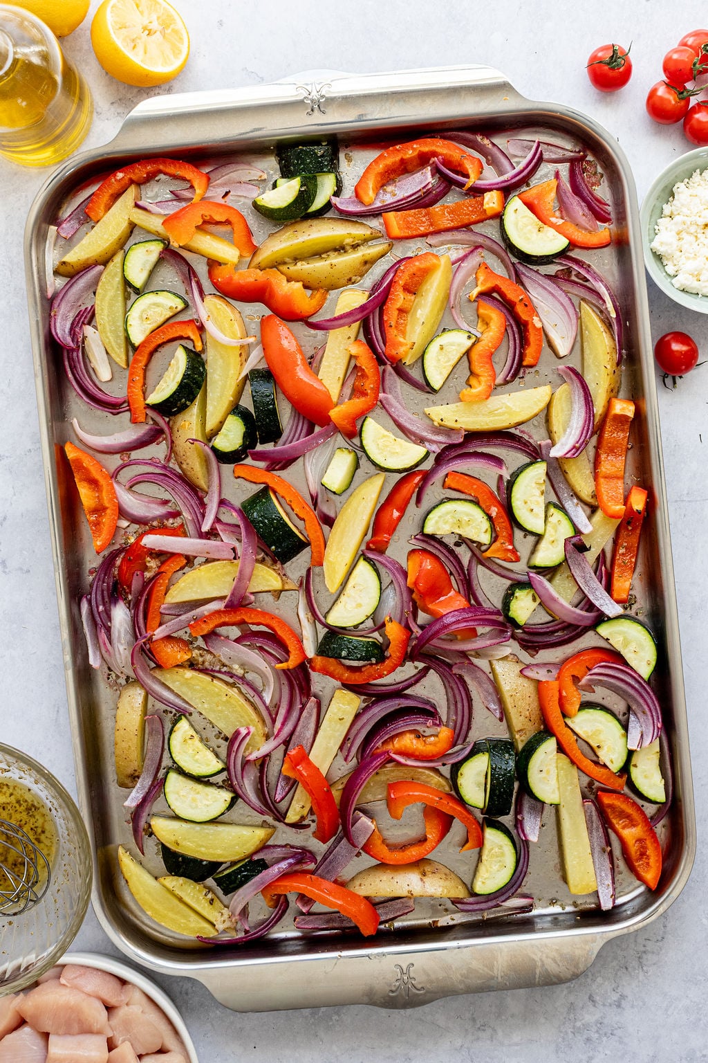 A baking sheet filled with sliced red onions, zucchini, red and yellow bell peppers, and potato strips.