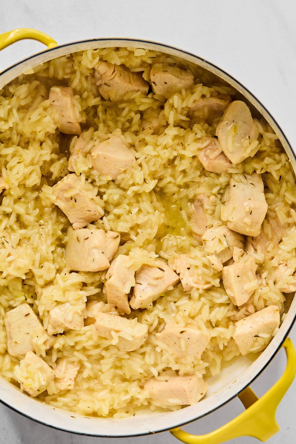 A pot filled with cooked yellow rice and chunks of chicken, viewed from above on a white surface.