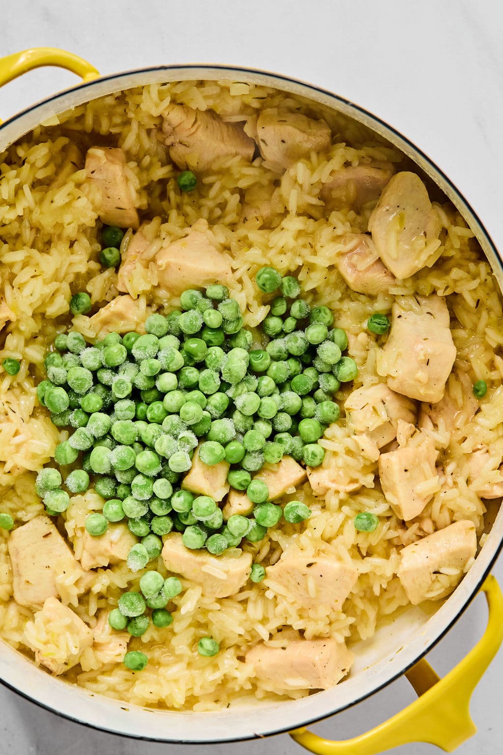 A pot of cooked yellow rice with pieces of chicken, topped with a mound of frozen green peas in the center.