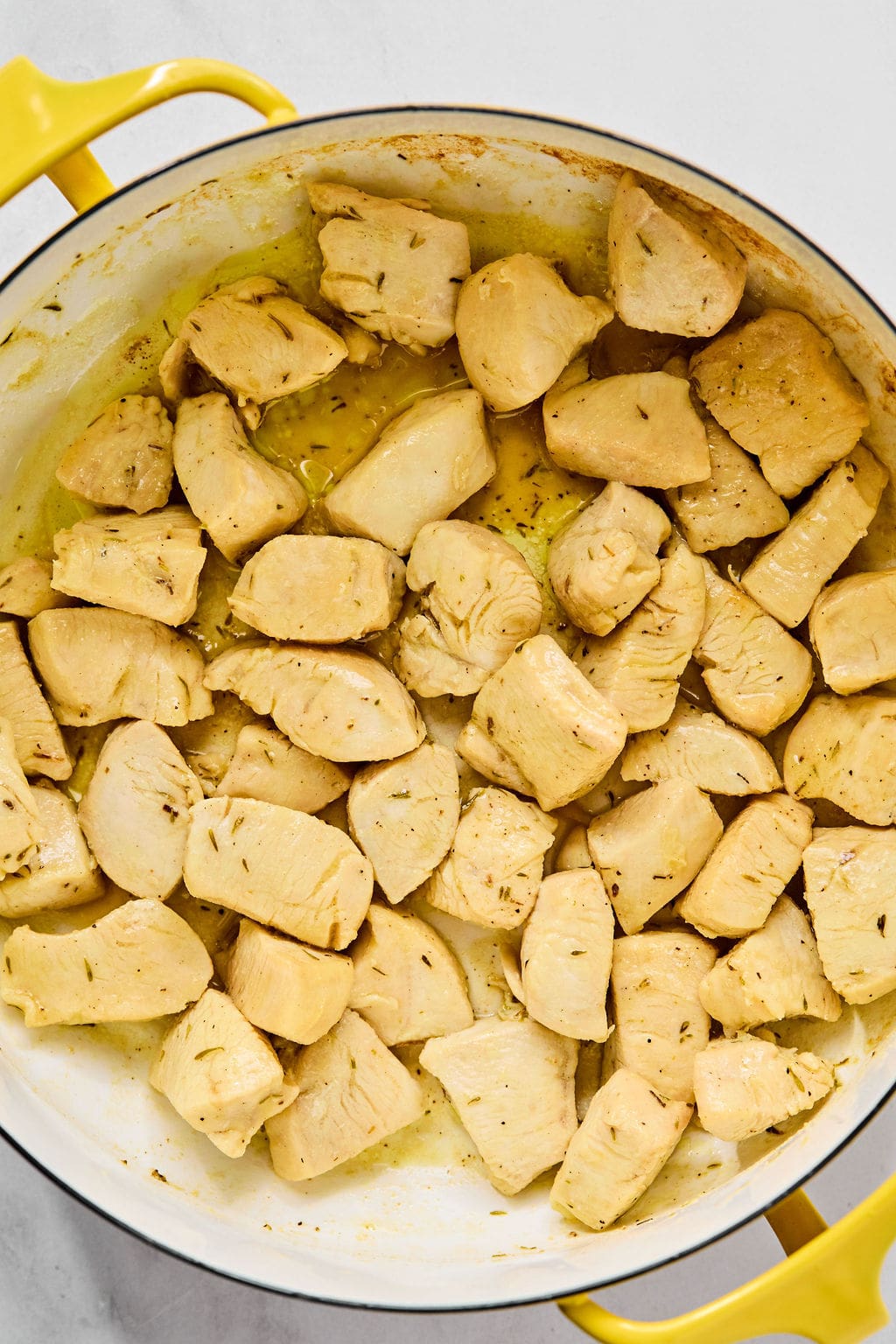 Cubed pieces of cooked chicken breast in a yellow frying pan with visible seasoning and oil.