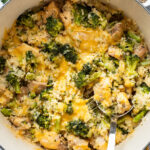 A pot filled with a broccoli, rice, and chicken casserole topped with melted cheddar cheese, with a serving spoon partially submerged.