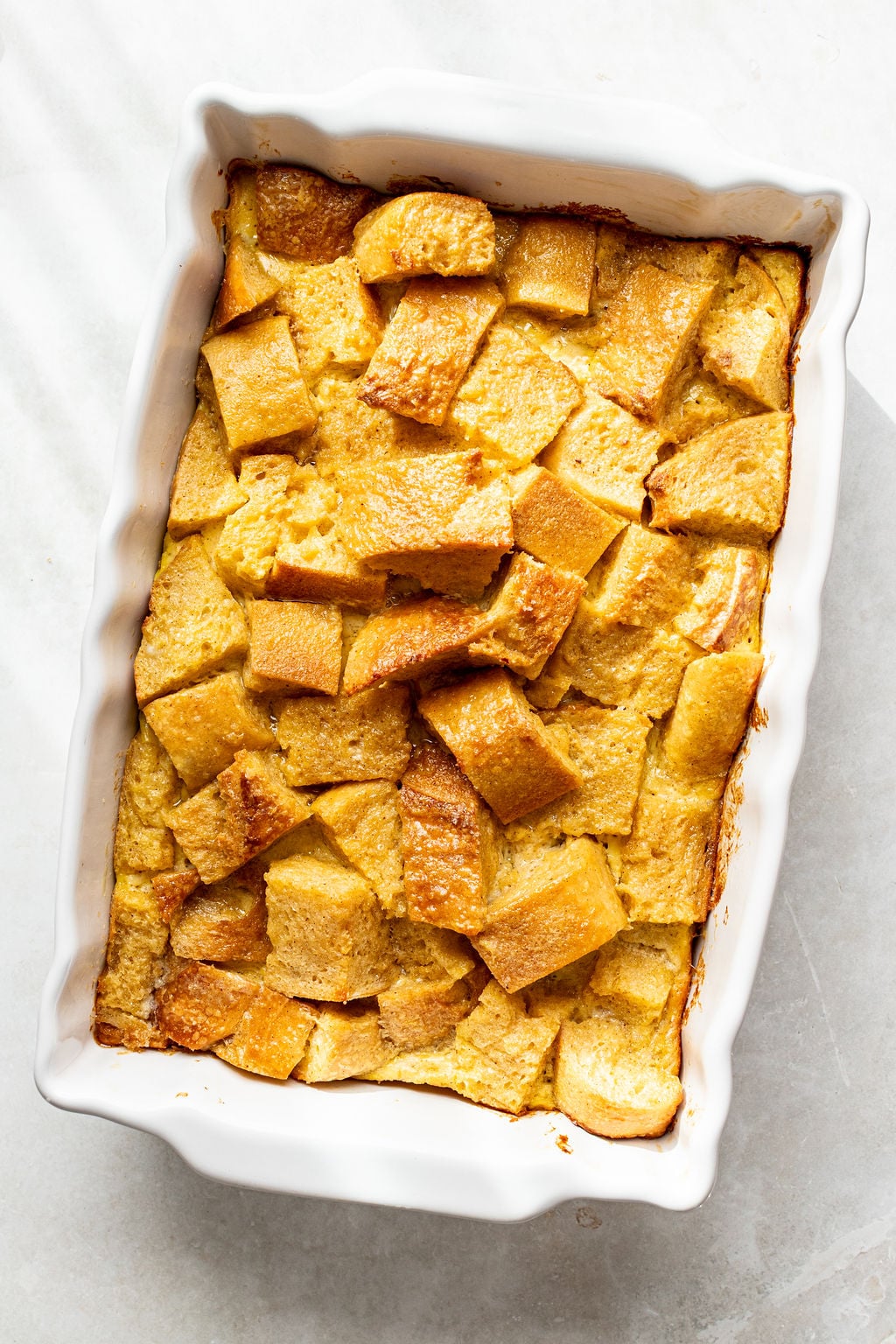 A white rectangular baking dish filled with baked bread pudding, featuring golden-brown, cubed pieces of bread.