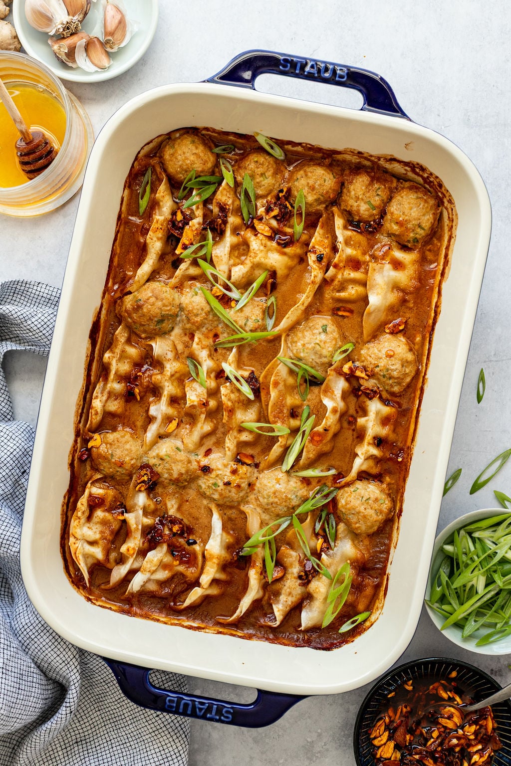A baking dish filled with baked dumplings and meatballs in a brown sauce, garnished with sliced green onions.