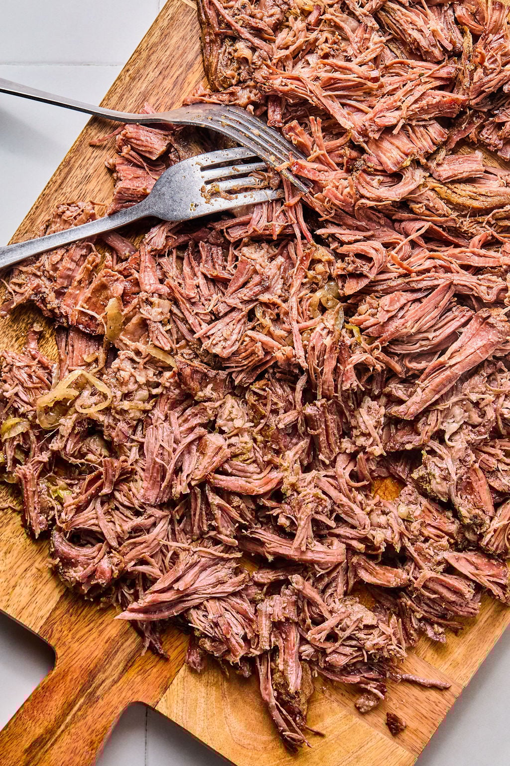 Shredded cooked beef spread on a wooden cutting board with a metal fork resting on top.