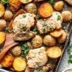 Baked chicken thighs and golden baby potatoes on a sheet pan, garnished with chopped parsley and grated cheese.