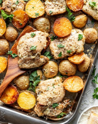 Baked chicken thighs and golden baby potatoes on a sheet pan, garnished with chopped parsley and grated cheese.
