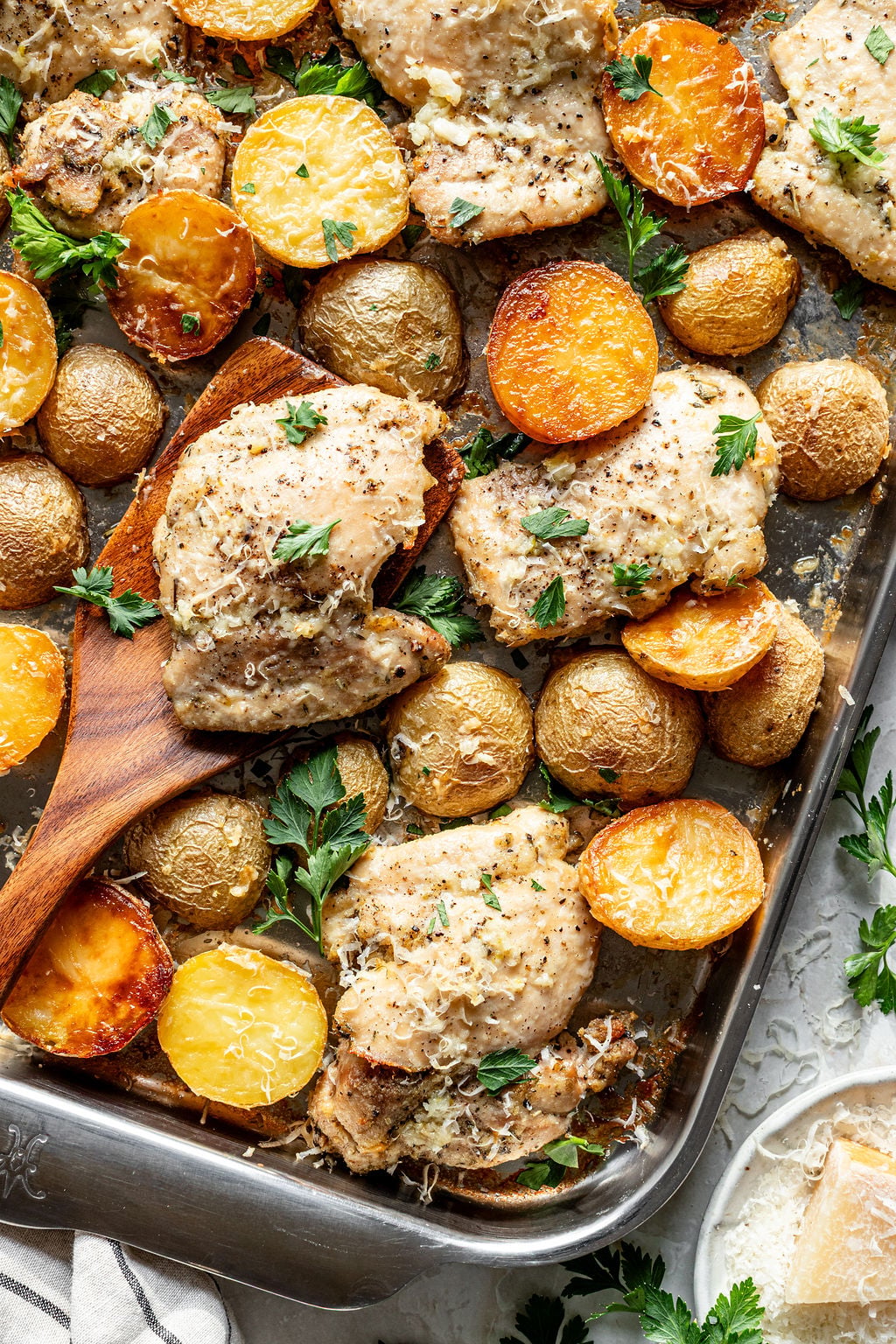 Baked chicken thighs and golden baby potatoes on a sheet pan, garnished with chopped parsley and grated cheese.