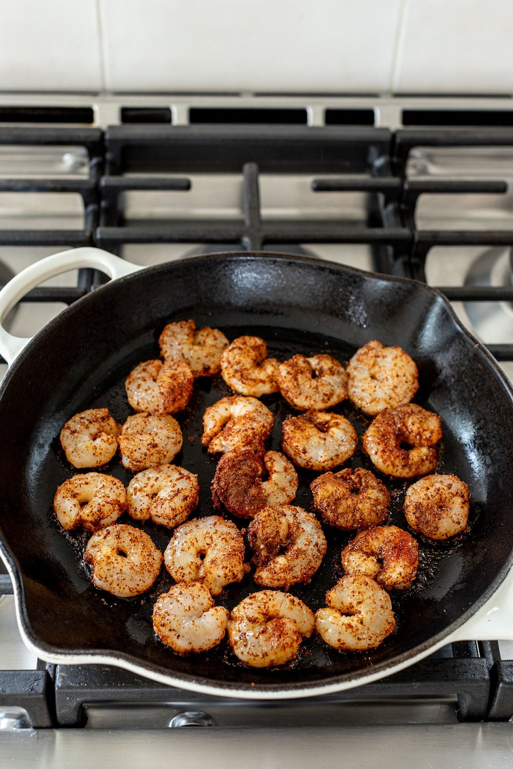 Shrimp seasoned with spices cooking in a black cast iron skillet on a gas stove.