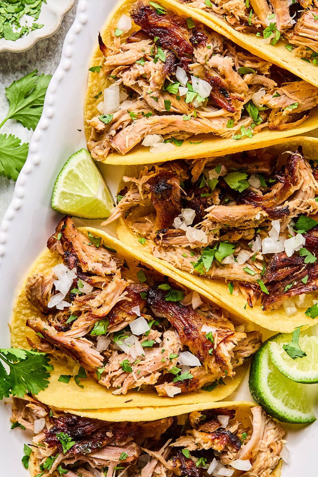 Three pork carnitas tacos served on corn tortillas, garnished with chopped onions and cilantro, with lime wedges on the side.