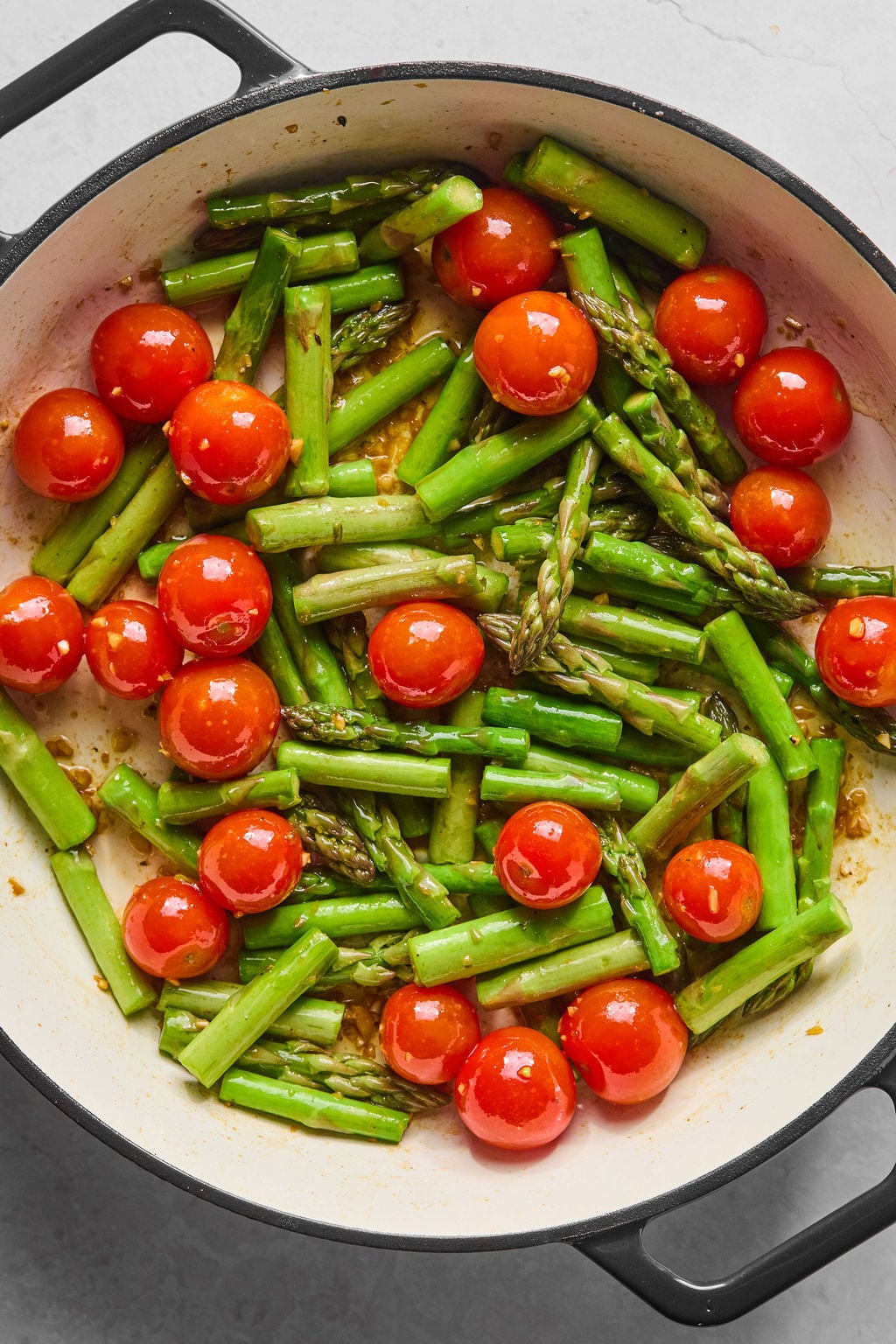 A pan filled with cooked asparagus spears and whole cherry tomatoes.