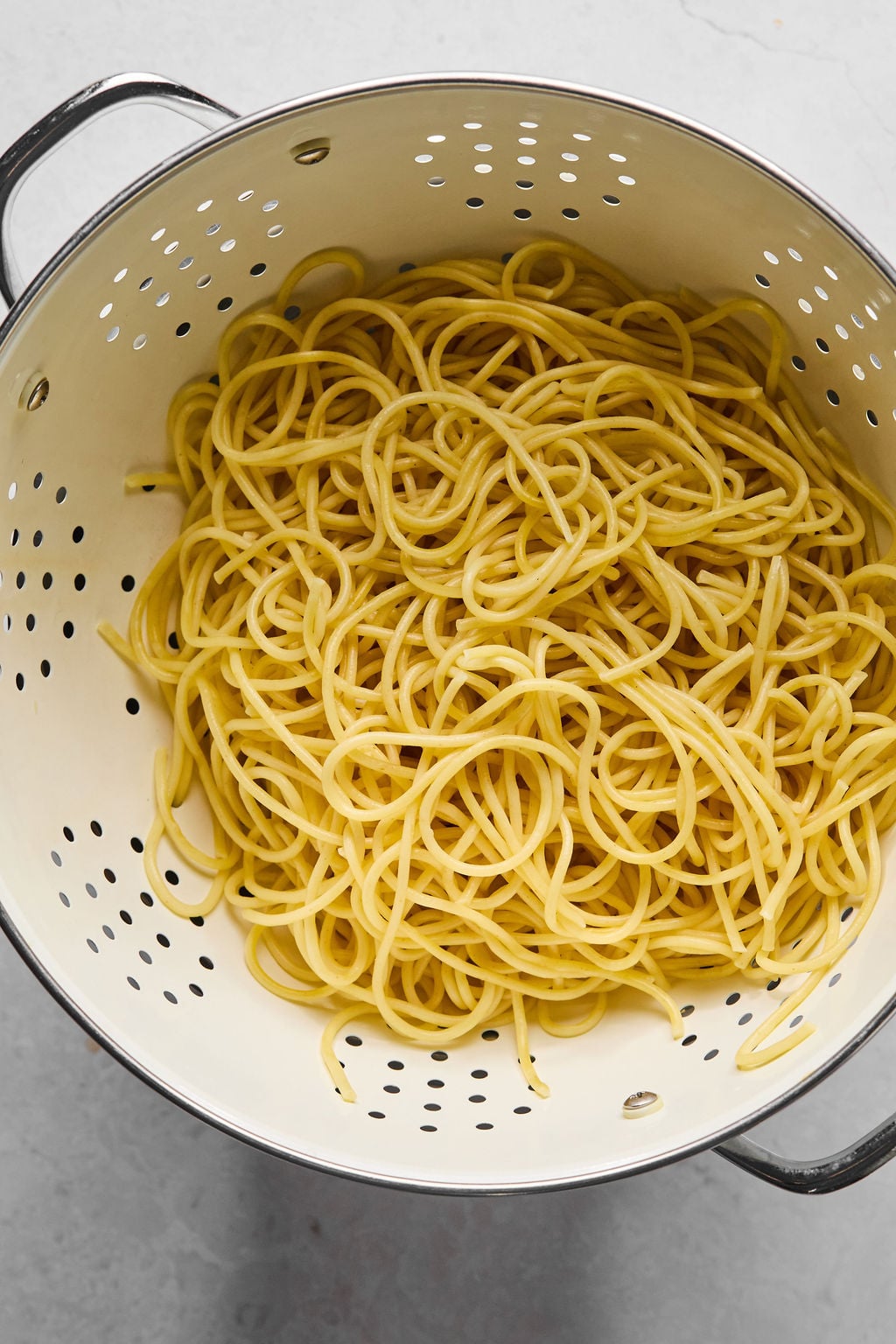 Cooked spaghetti noodles draining in a white metal colander.
