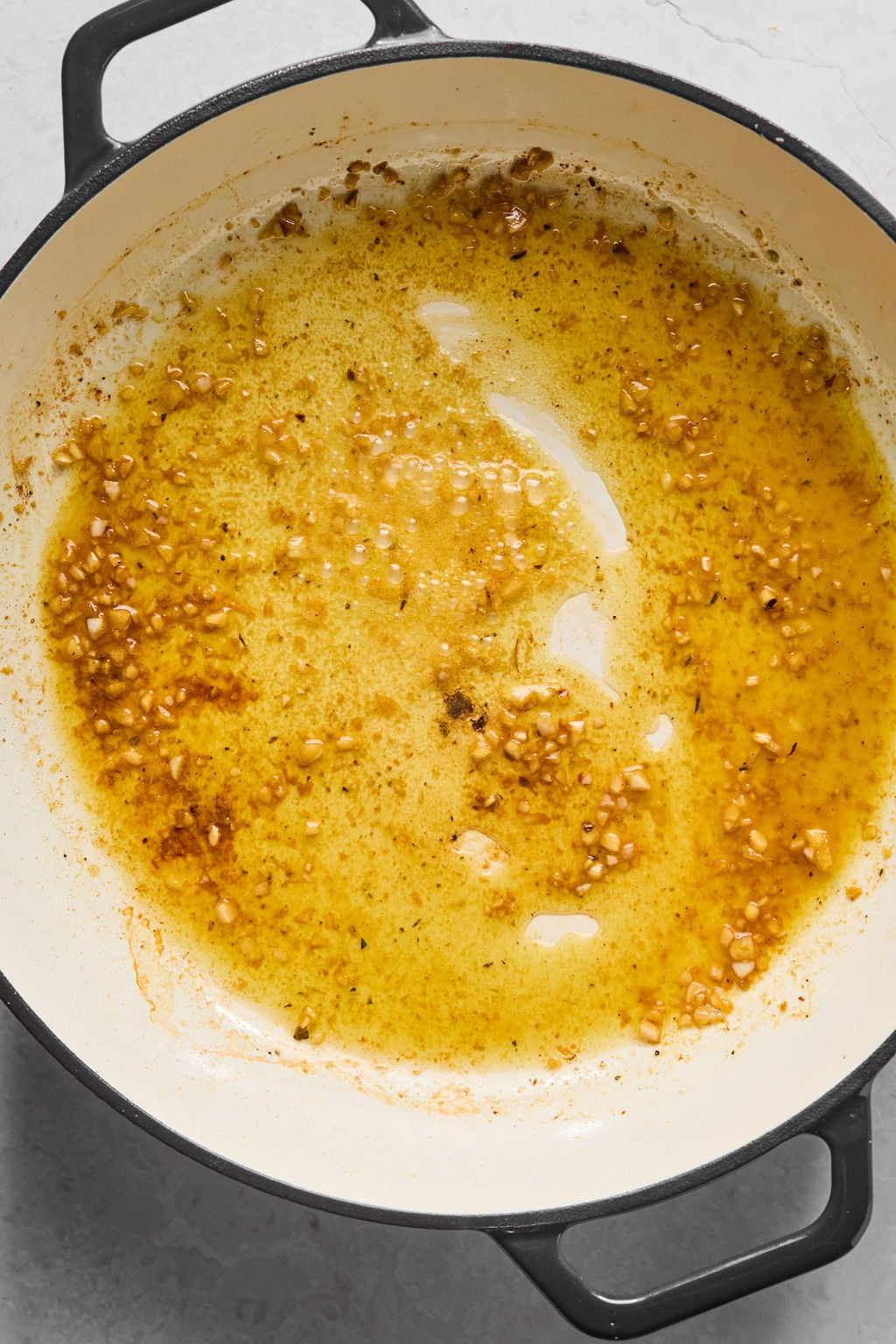 A Dutch oven with browned bits and saut&eacute;ed minced garlic in oil on the bottom, showing the initial stage of cooking.