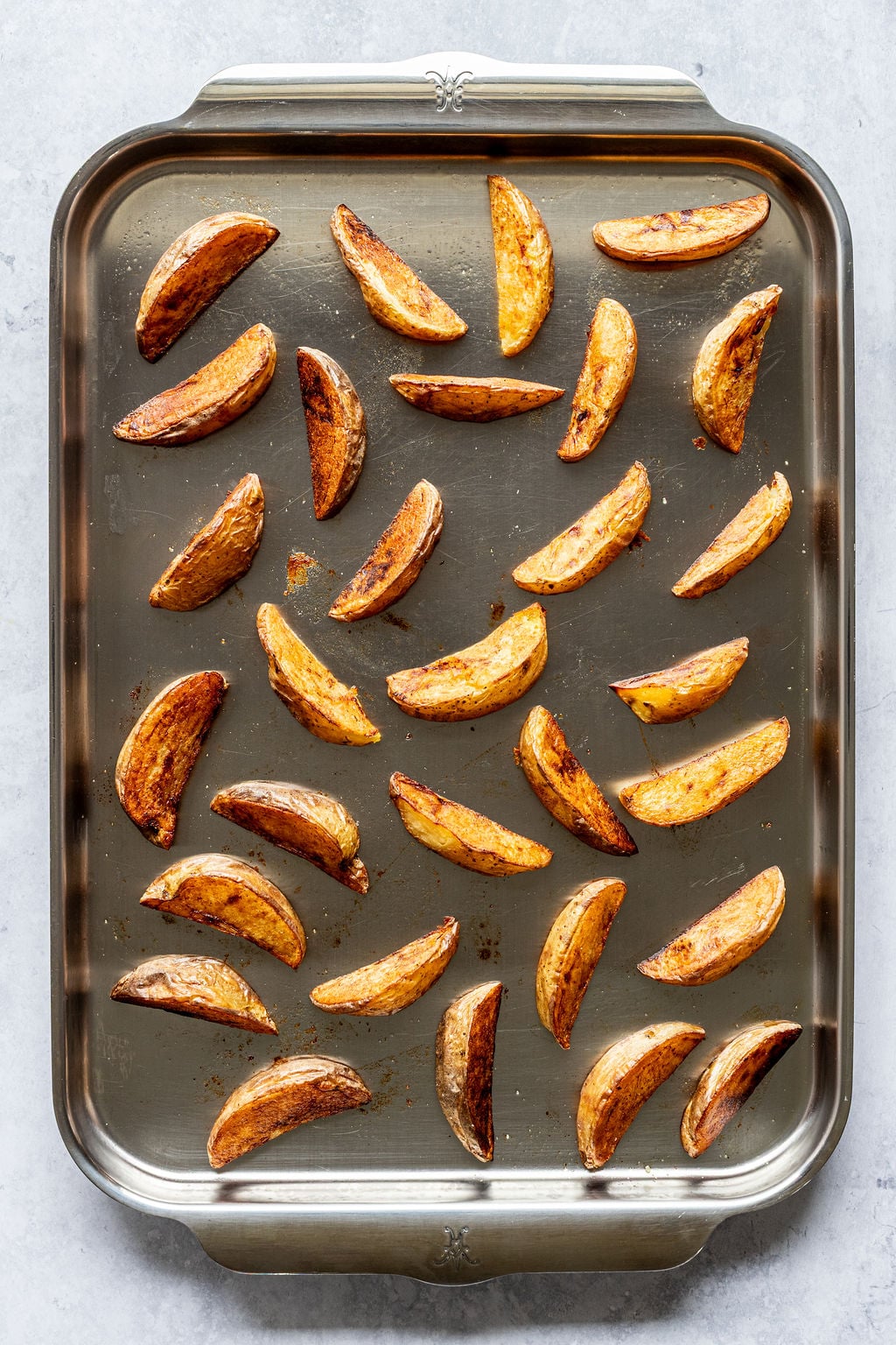 Baked potato wedges arranged in rows on a metal baking sheet.
