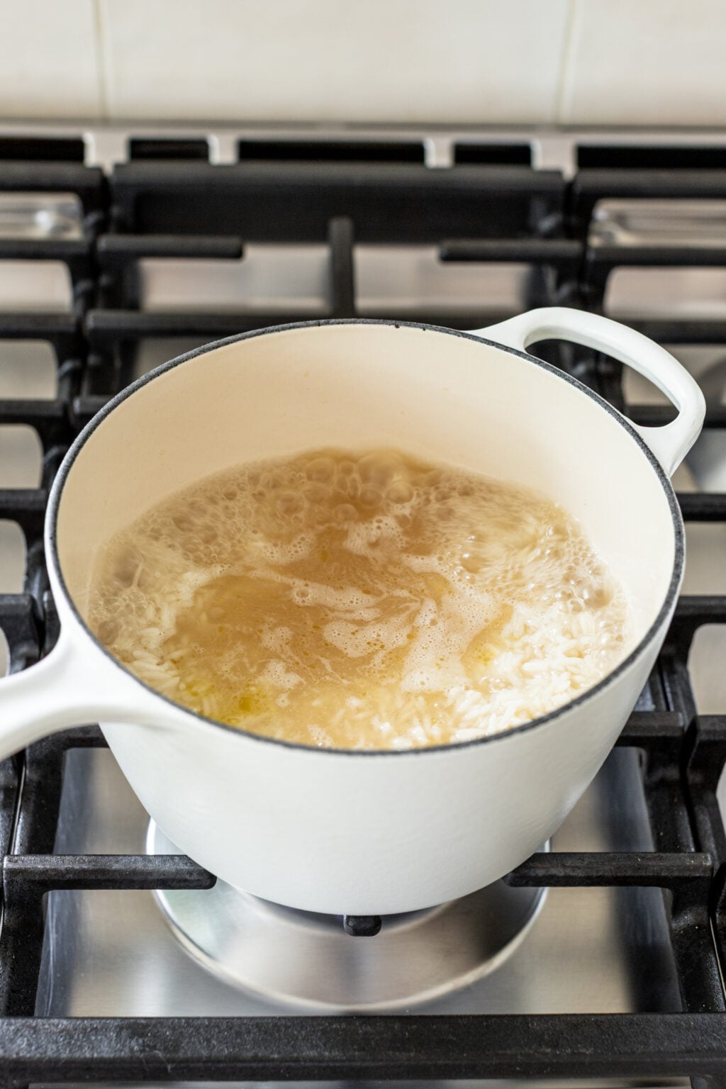 A white pot with boiling water and rice sits on a gas stove burner.