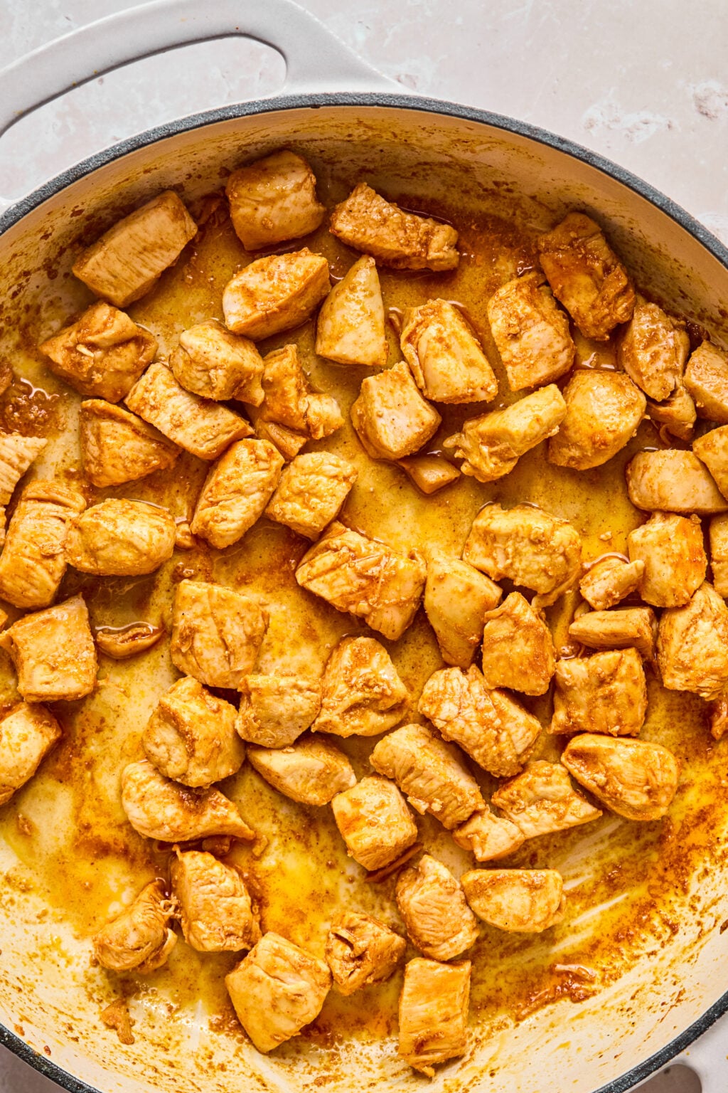 Cubed pieces of cooked chicken breast are saut&eacute;ed in a large pan, coated with a light brown seasoning or sauce.