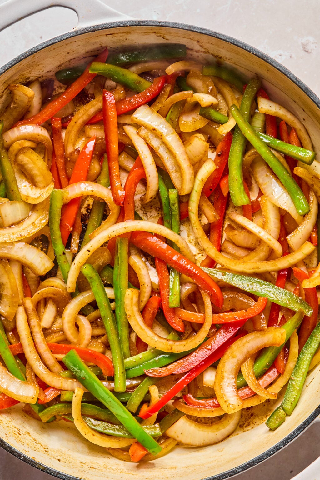 Sliced onions, red bell peppers, and green bell peppers being saut&eacute;ed in a large pan.