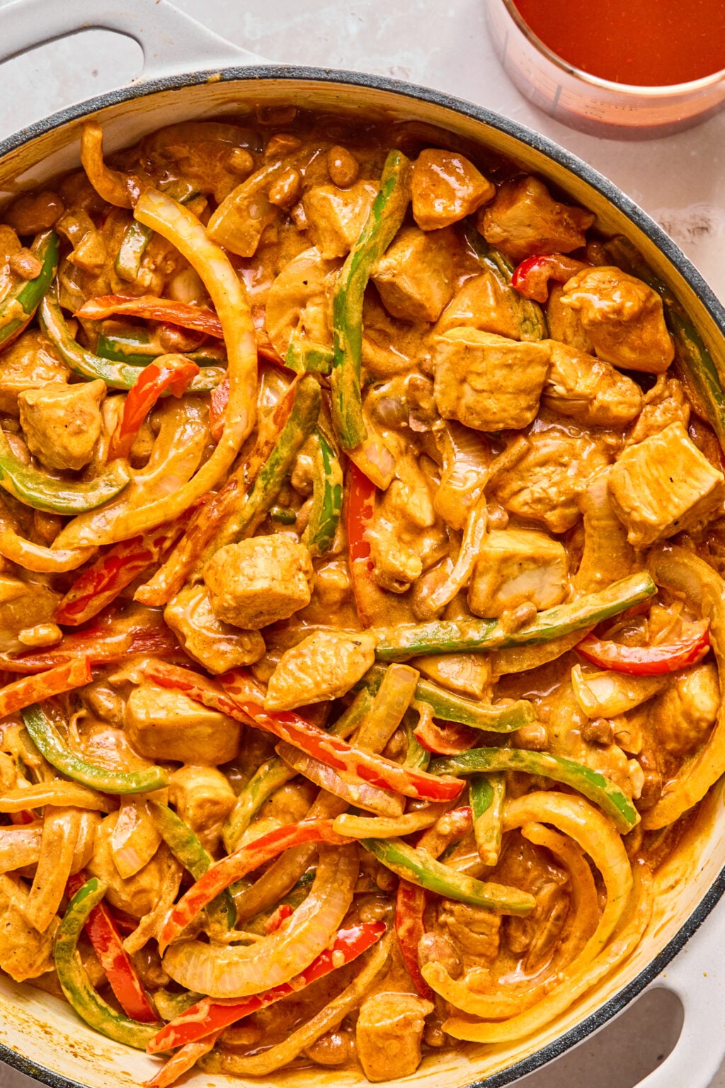 A skillet filled with a creamy sauce featuring chunks of meat, sliced onions, and red and green bell peppers.