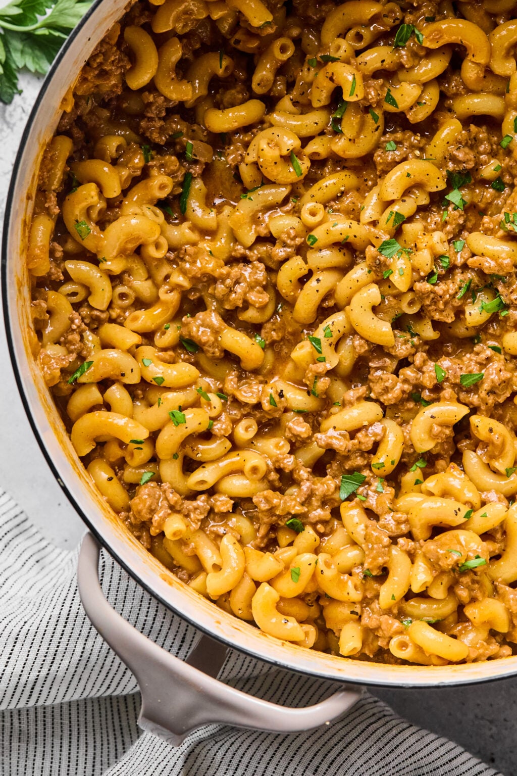 A large pot filled with macaroni pasta mixed with ground beef and garnished with chopped parsley.