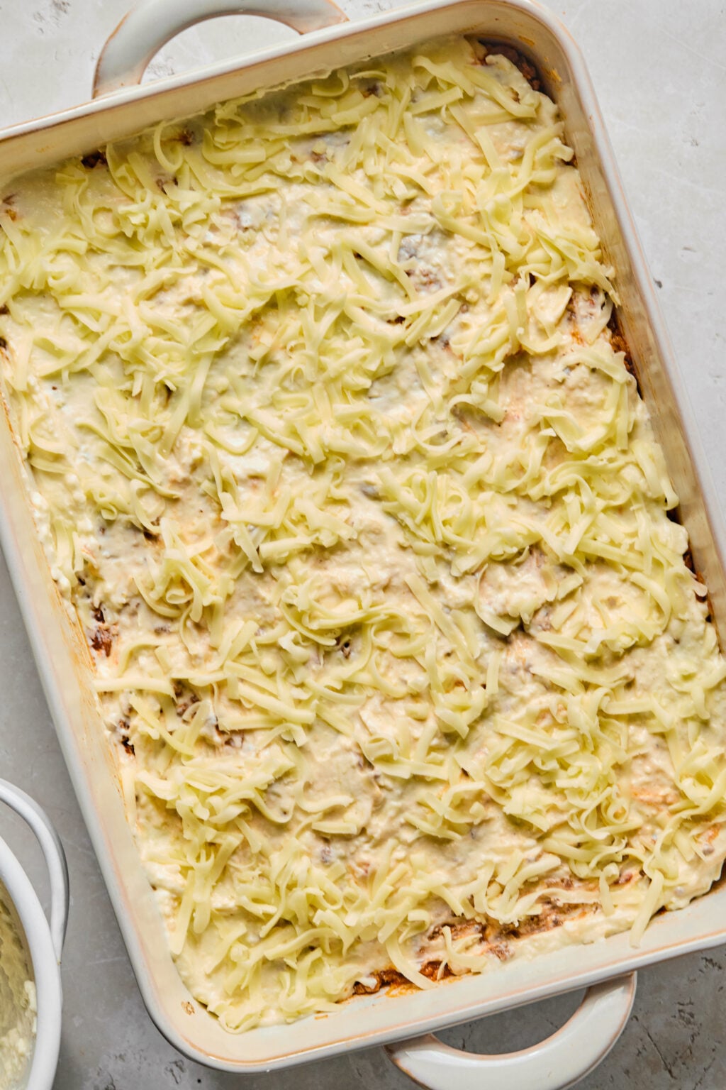 A rectangular baking dish filled with a casserole topped with melted and shredded cheese, sitting on a light-colored countertop.
