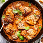 Chicken thighs simmered in a creamy tomato sauce with herbs, garnished with fresh basil leaves in a black skillet.